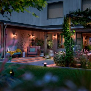 Outdoor wall lights and pathway lights installed in backyard, illuminating patio seating area and garden plants with soft lighting.