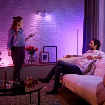 A couple relax in their living room with Philips Hue holiday lighting that fills their space with shades of blue and purple smart light. 