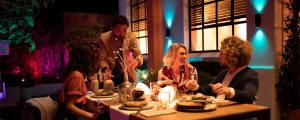 Group dining outdoors at night with colorful smart lighting illuminating the garden and wall, enhancing the dinner setting.