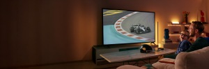 Ein Vater und sein Sohn lächeln, während sie sich ein rasantes Autorennen im Fernsehen ansehen, mit WiZ Smart Lighting hinter dem Bildschirm und in den nahe gelegenen Regalen.