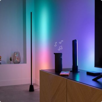 En Gradient gulvlampe, en Gradient light bar og en TV-lightstrip, projicerer alle lys, der er synkroniseret med musik, der afspilles fra en højttaler i en moderne stue.