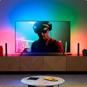 Sistema de TV en una sala de estar con Gradient Light Bars a ambos lados del televisor, que proyectan diferentes colores que cambian con la pantalla del televisor y están sincronizados con la TV Backlight.