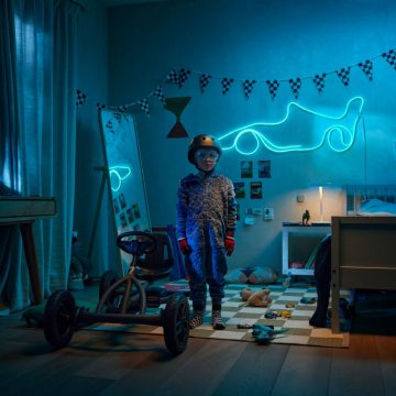 Un băiat stă lângă un kart în camera sa cu tematică de curse, iluminată de o bandă WiZ Smart Flex, albastră, în formă de mașină de curse.